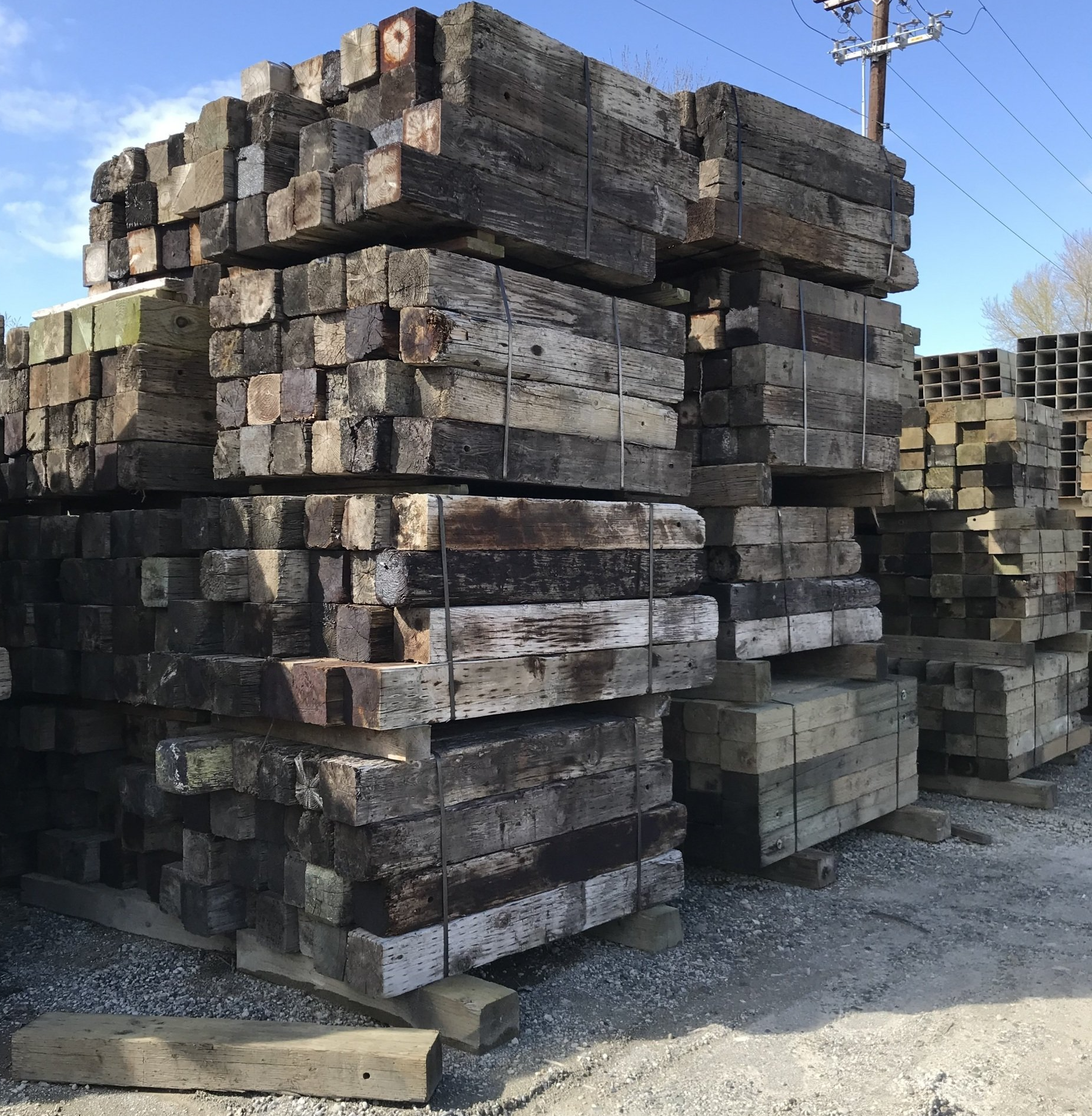 Stacks of weathered wooden railroad ties, bundled together, outdoors on a sunny day.