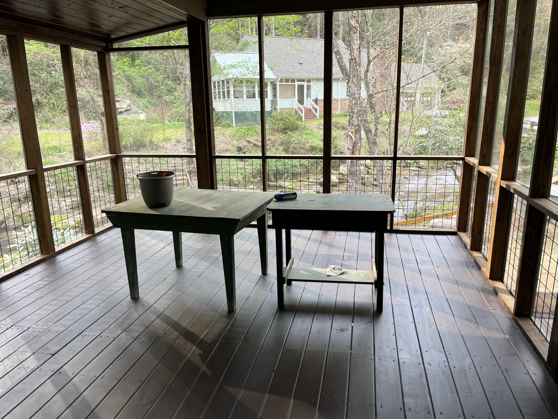A screened in porch with two tables and a house in the background.