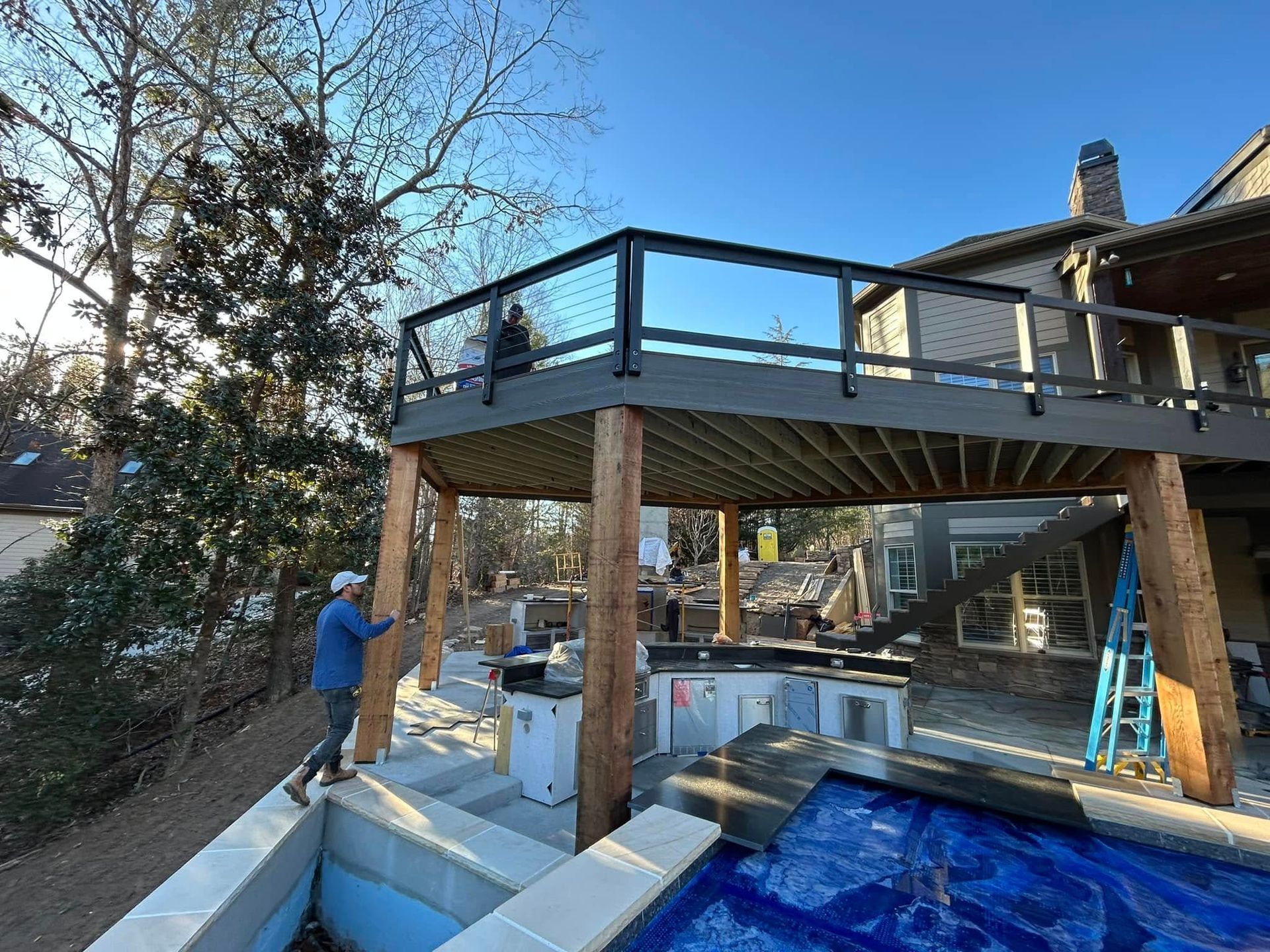 A man is standing on top of a wooden deck overlooking a swimming pool.