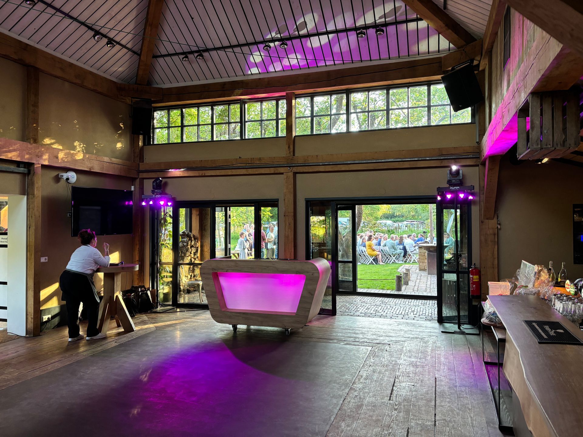 Modern interieur van de lodge met paarse verlichting, een centrale receptiebalie en grote glazen deuren die uitkomen op een tuin.