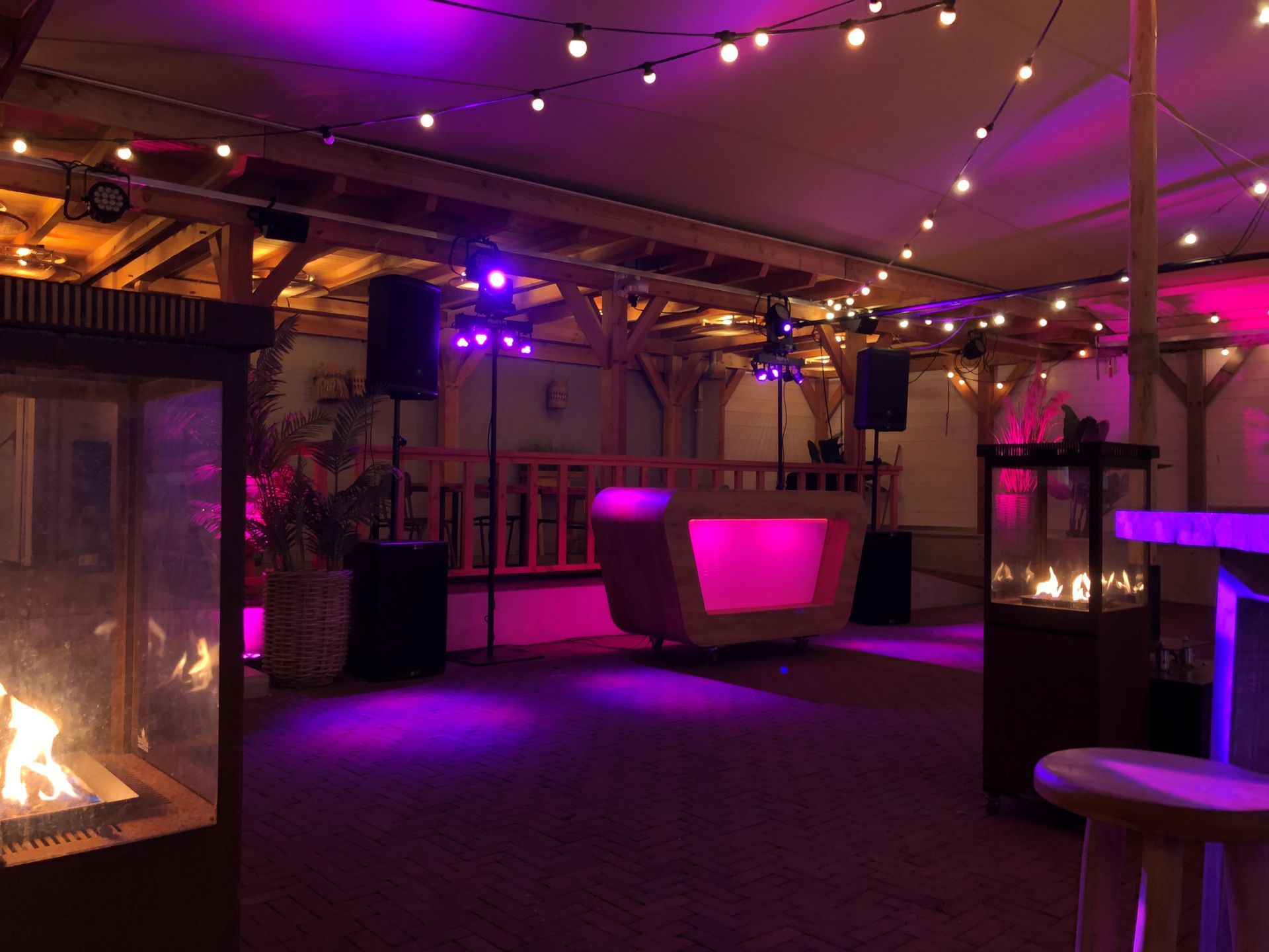 Paars verlichte binnenlounge met lichtslingers, een sfeervolle bar en een open haard na zonsondergang.