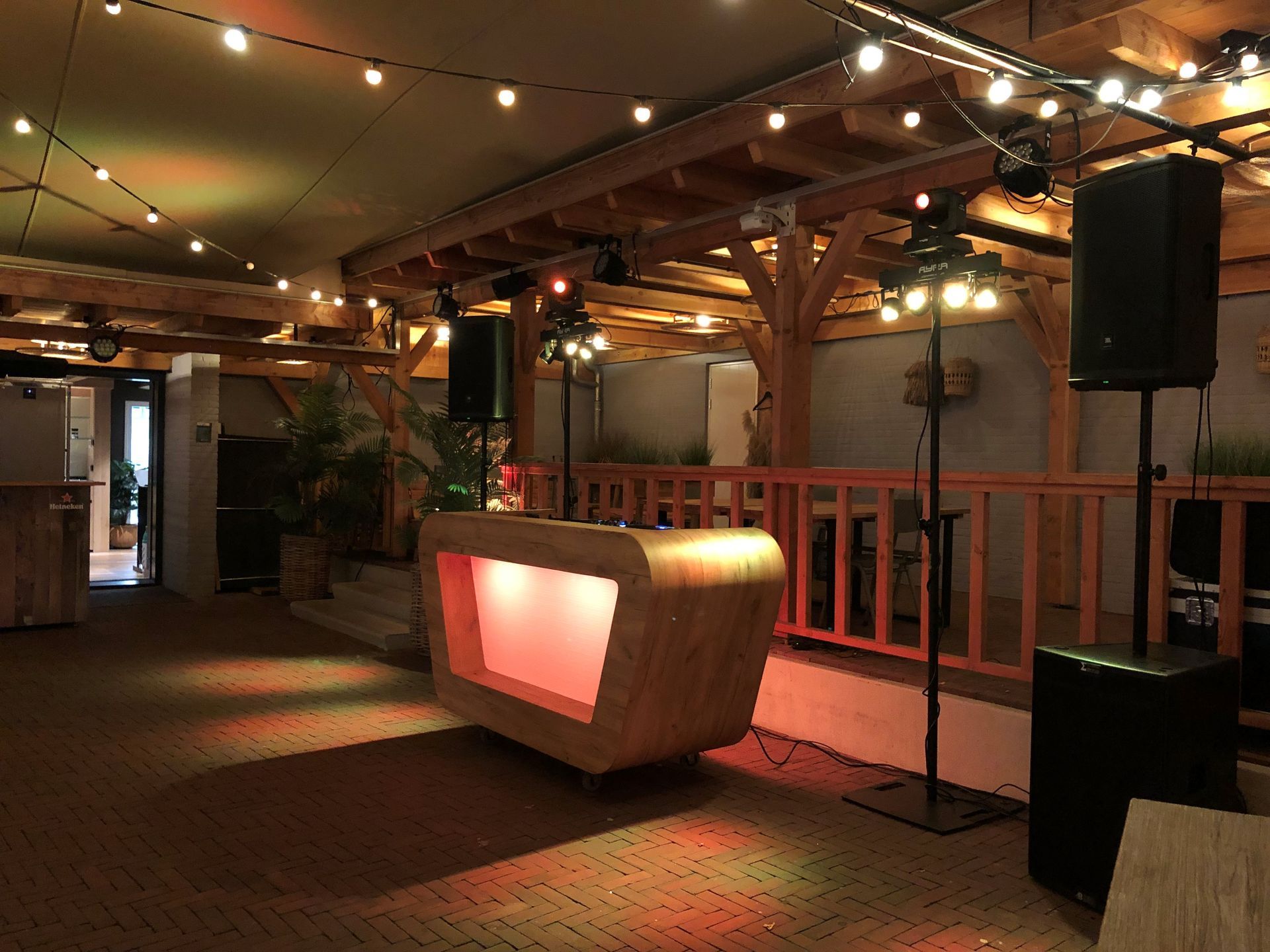 Sfeervol verlichte binnenlounge met een verlichte bar, lichtslingers en een grote luidspreker aan de rechterkant.