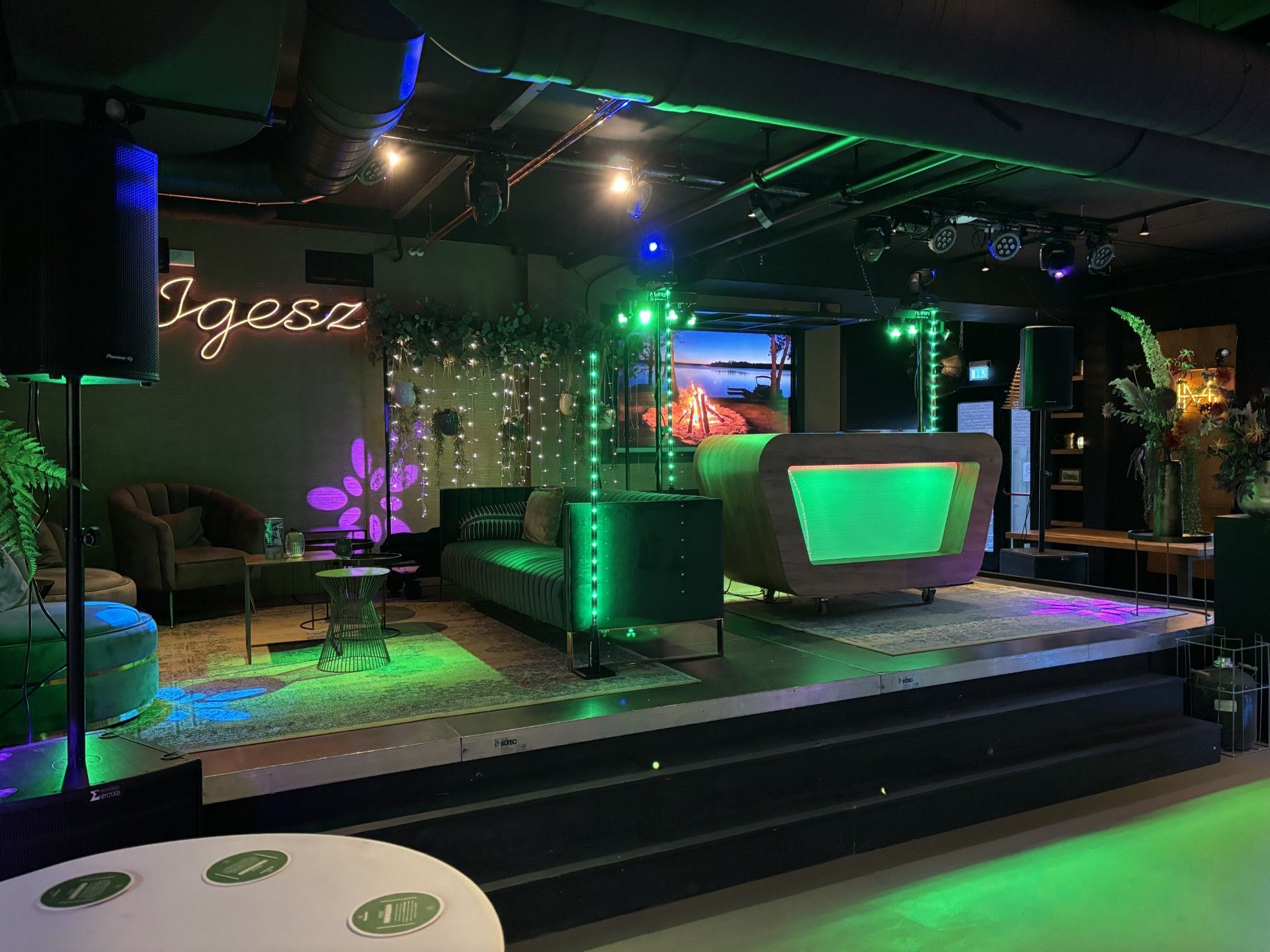 Een loungepodium met neonverlichting, een gebogen bar, groene accentverlichting en een paarse, stralende kerstboomversiering.