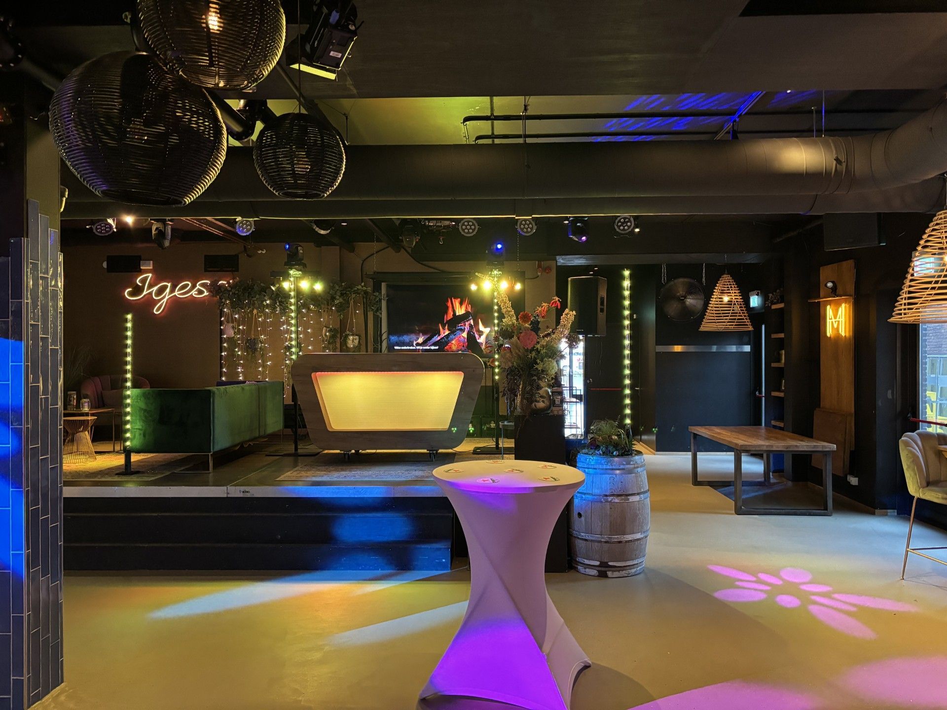 Een schemerig verlichte lounge met sfeervolle cocktailtafels, dansvloerverlichting en een bar op de achtergrond.
