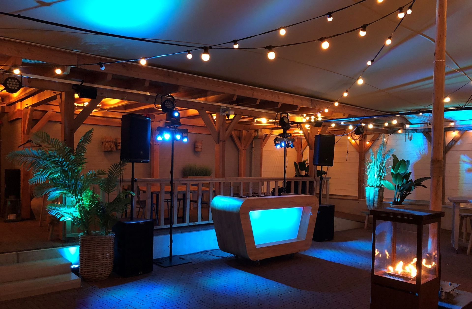 Buitenlounge op het terras met lichtslingers, een sfeervolle bar, palmbomen in potten en warme blauw-oranje sfeerverlichting.