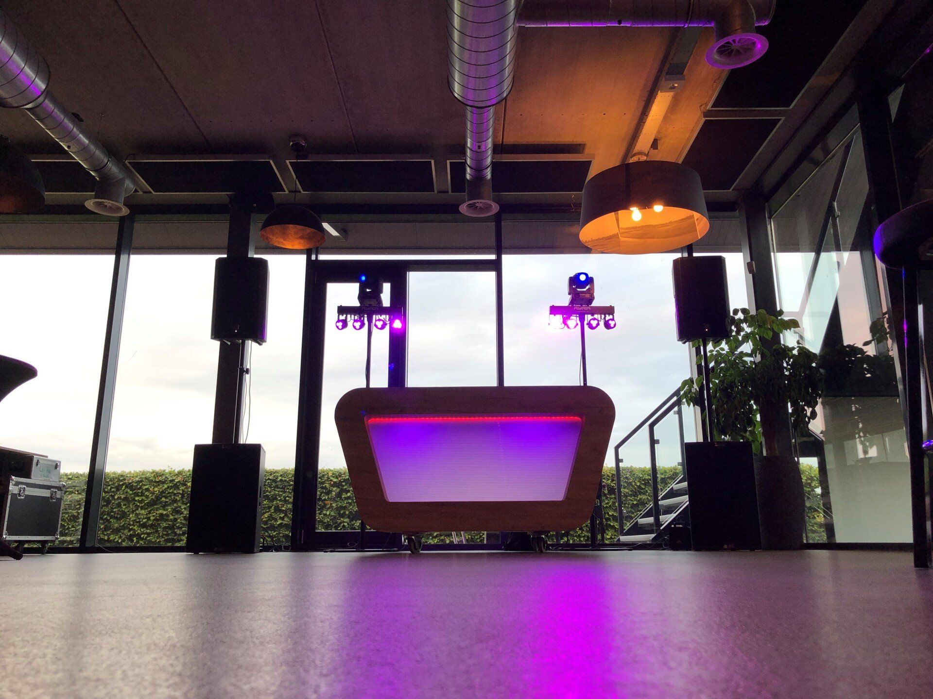 Moderne lounge met paars verlichte tafel, grote ramen en hanglampen met uitzicht op de stad.