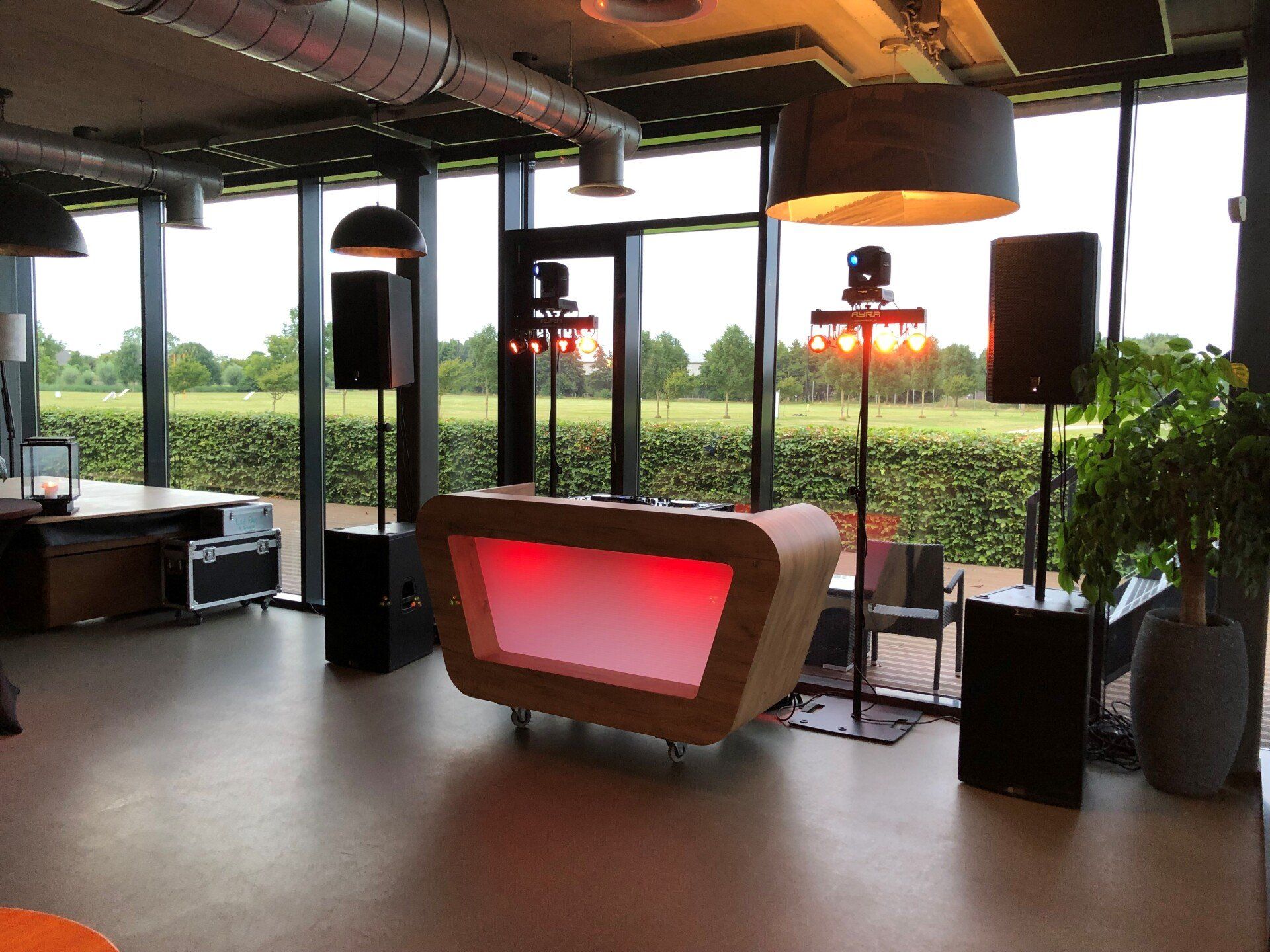 Moderne lounge met grote ramen, rood verlichte bar, speakers en uitzicht op de stad en het groen.