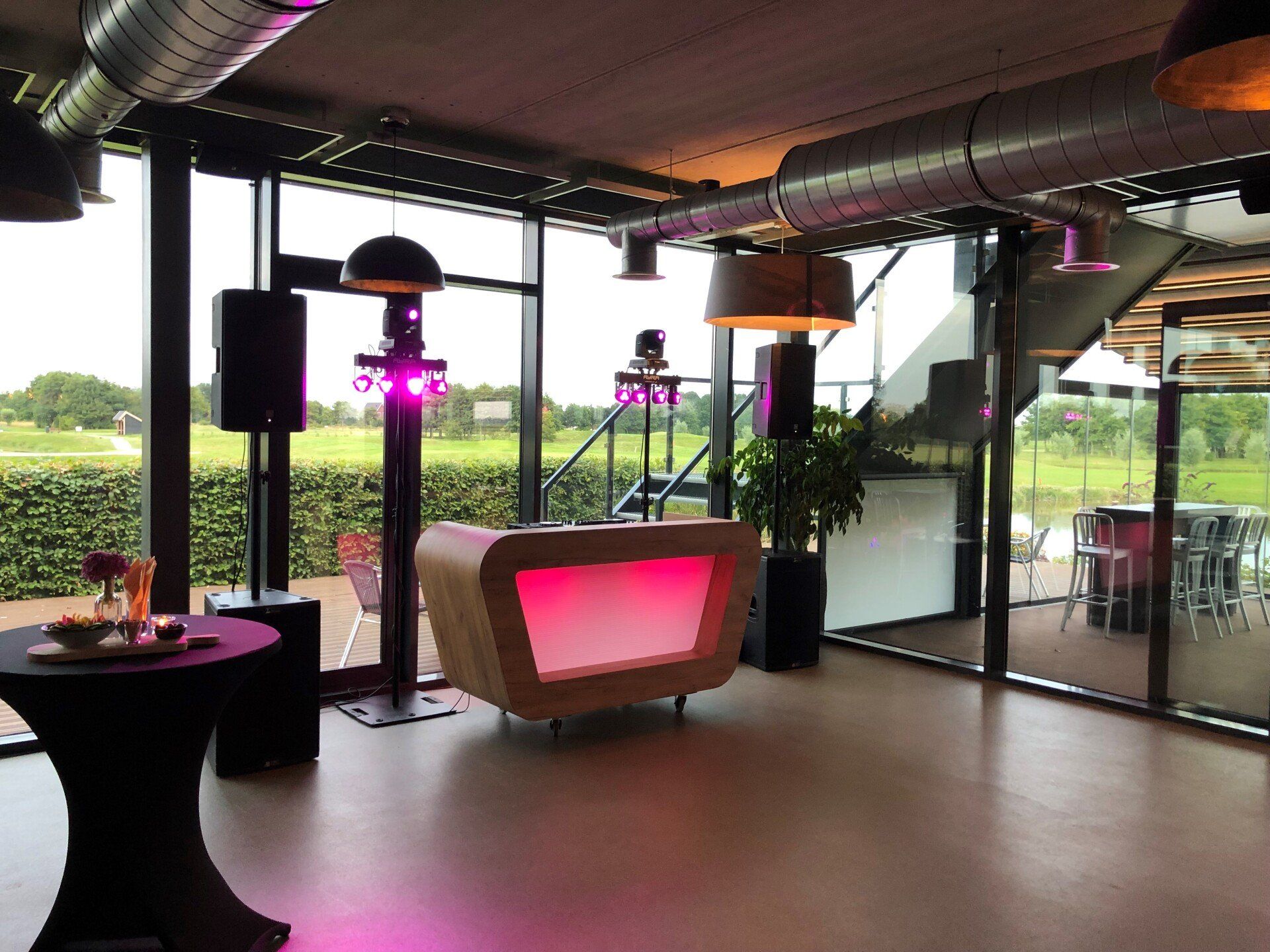 Binnenterrasbar met sfeervolle roze terraslampen en moderne tafels met uitzicht op de tuin.