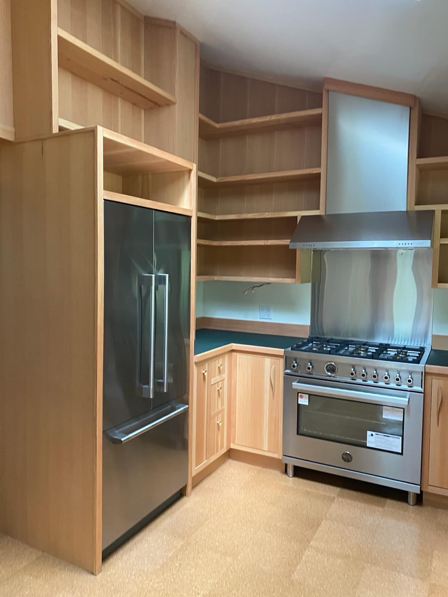 A light-wood kitchen featuring an open-shelf design, stainless steel refrigerator, professional range, and hood vent.