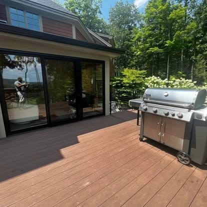 Back deck with a stainless gas grill beside sliding glass doors and trees beyond