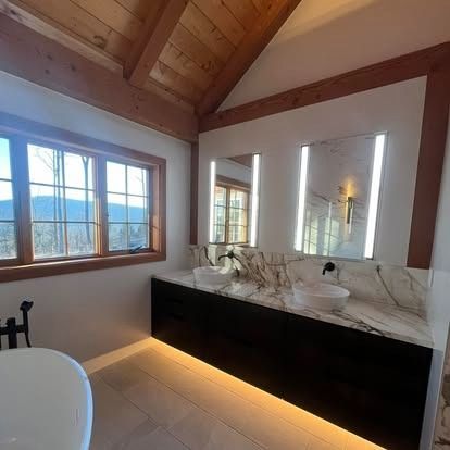 Wooden-beamed bathroom with mountain-view window, marble vanity, large mirror, and black cabinetry.