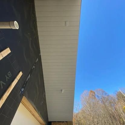 Low-angle view of a white, paneled exterior ceiling soffit under a clear blue sky, next to a black building exterior.