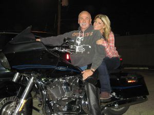 Two people posing on a black motorcycle at night, smiling toward the camera.