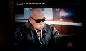 Man in sunglasses and leather jacket singing into a microphone on a stage
