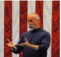 Man gesturing with both hands in front of a red-and-white striped backdrop