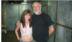 Two people standing together in a metallic room, one in a pink top and one in a black shirt.