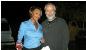 Two people standing together at night, smiling; woman in blue shirt, man in dark jacket.