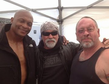 Three men posing together under a white canopy, smiling at the camera.