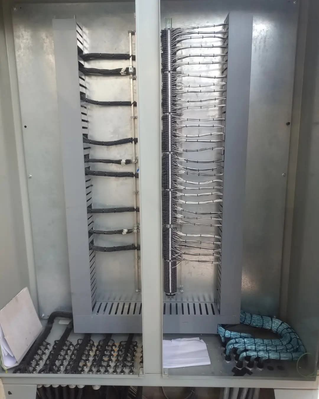 Armario eléctrico abierto con filas de paneles de interruptores y cableado dentro de una carcasa metálica gris.