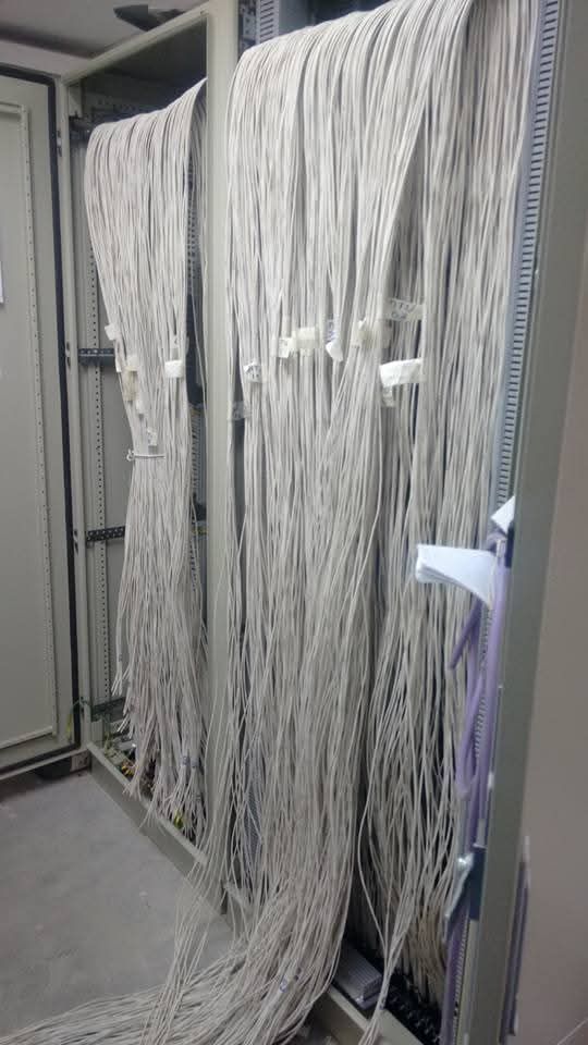 Manojos de cables blancos colgando dentro de un armario eléctrico abierto.