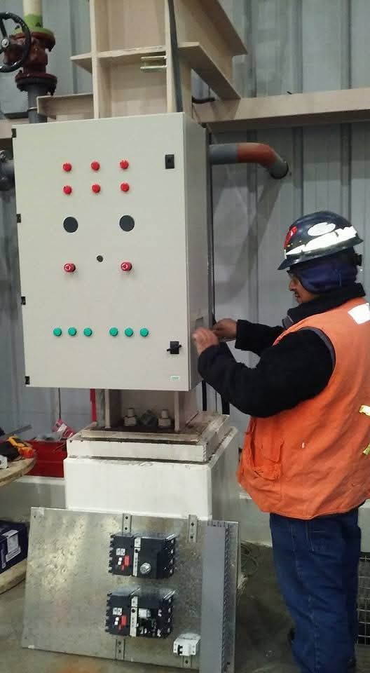 Un trabajador con casco opera un panel de control industrial con botones rojos y verdes en una fábrica.