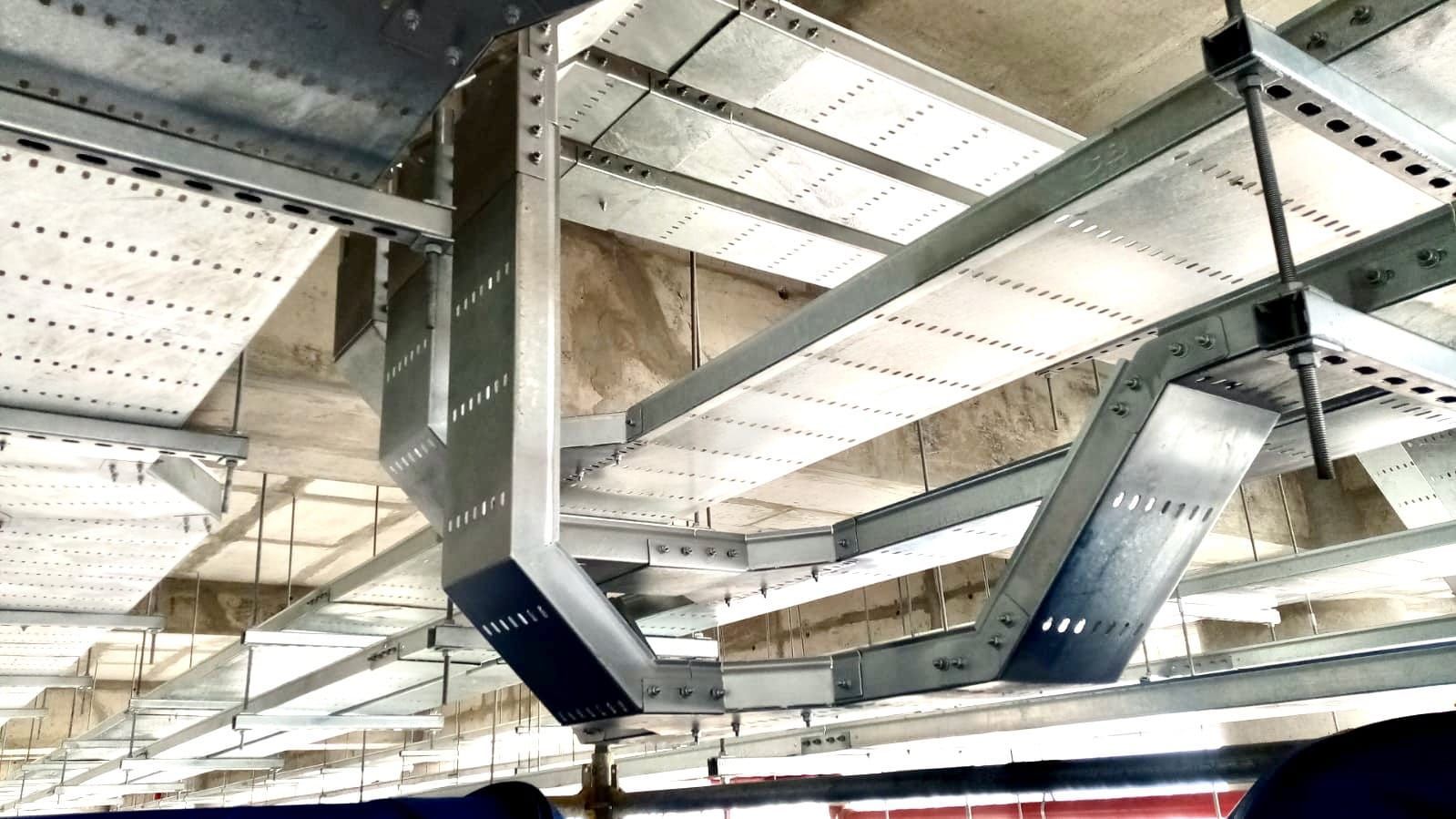 Conductos y vigas metálicas en el techo de un interior industrial, con soportes azules.