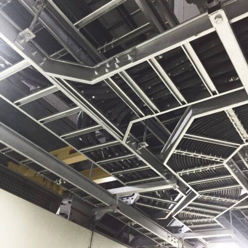 Parte inferior de una estructura de techo metálica con vigas y rejillas expuestas en un interior industrial.