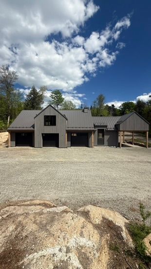 Maison grise moderne avec des boiseries foncées, un garage pour trois voitures et une allée en gravier.
