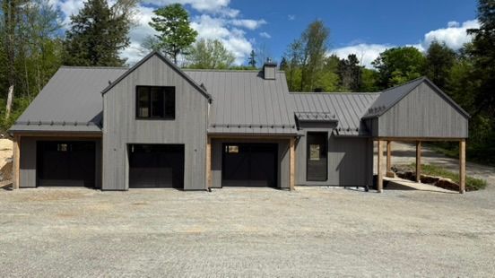 Maison moderne grise avec trois portes de garage et une entrée couverte. Allée en gravier.