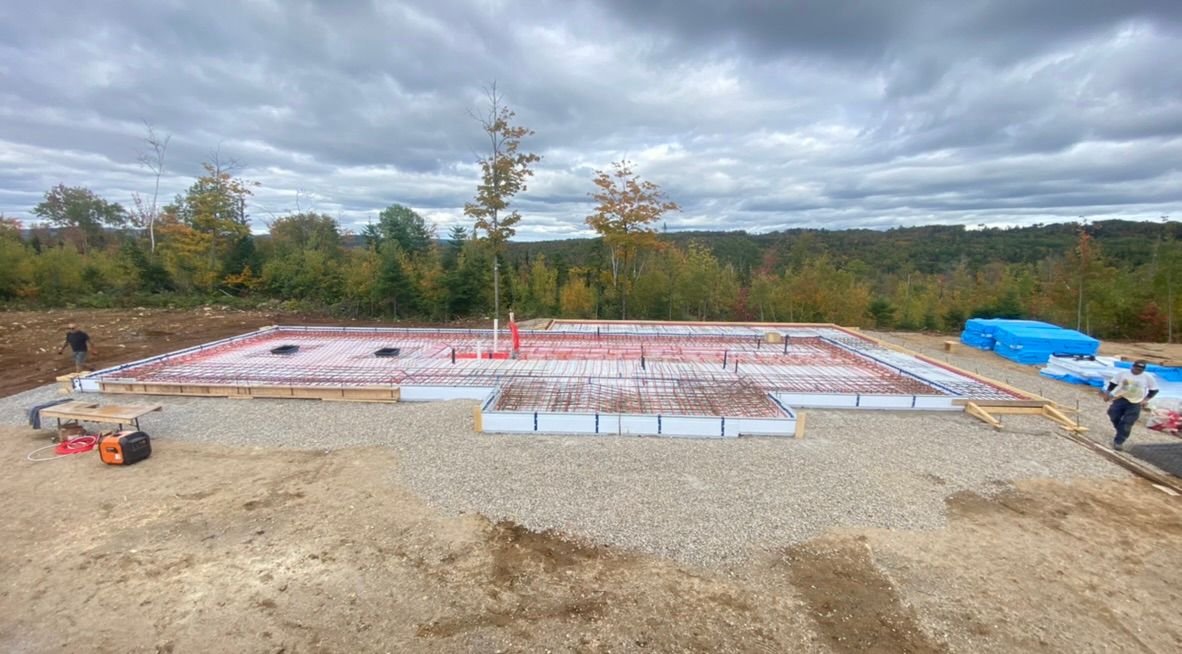 Chantier de construction avec gravier, fondations en armature et ciel nuageux.