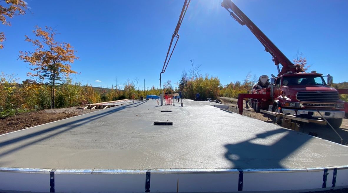 Du béton est coulé à l'aide d'un camion-pompe sur une dalle de béton fraîche par une journée ensoleillée.