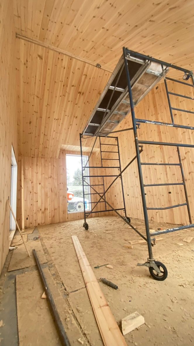 Vue intérieure d'une pièce en construction avec lambris, échafaudage et fenêtre.