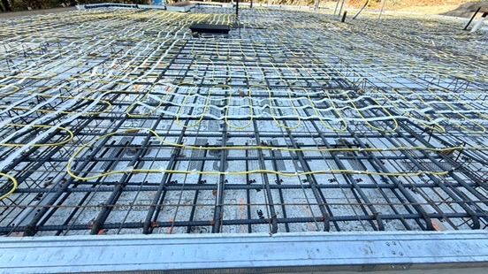 Fondation en béton armé avec une grille de barres d'armature et des tubes de chauffage radiant jaunes.