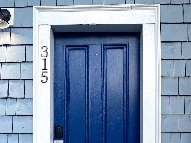Blue front door with house number 315 on a light blue shingled house.