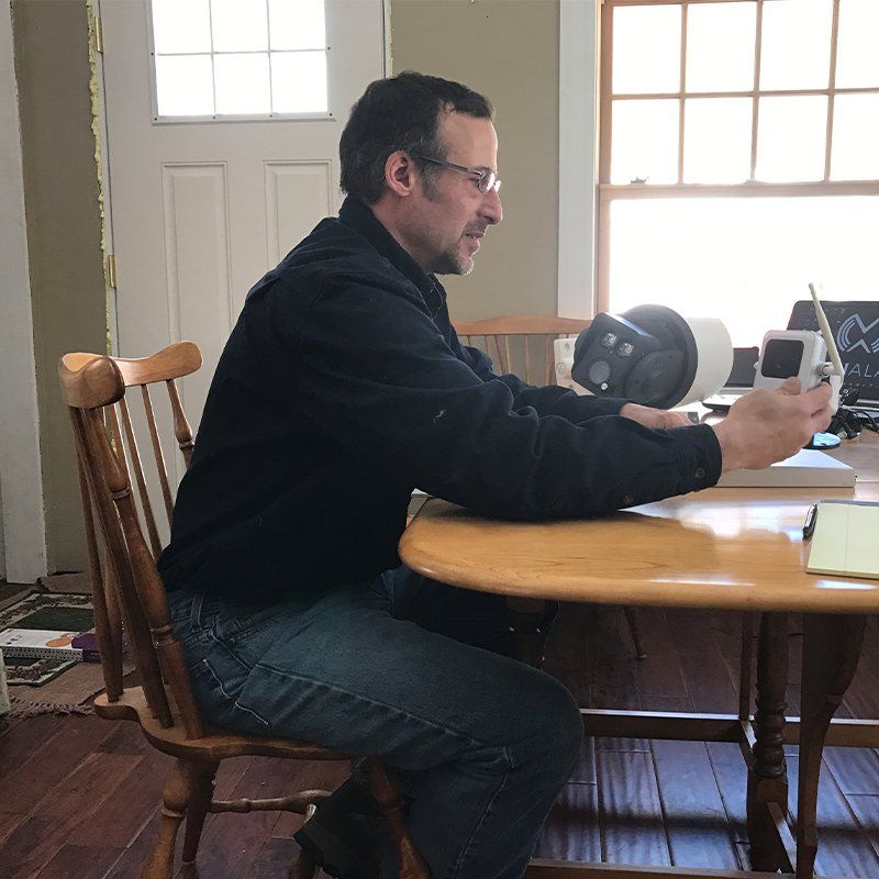 Man seated at table holding a small object, near a window and an opaque object.