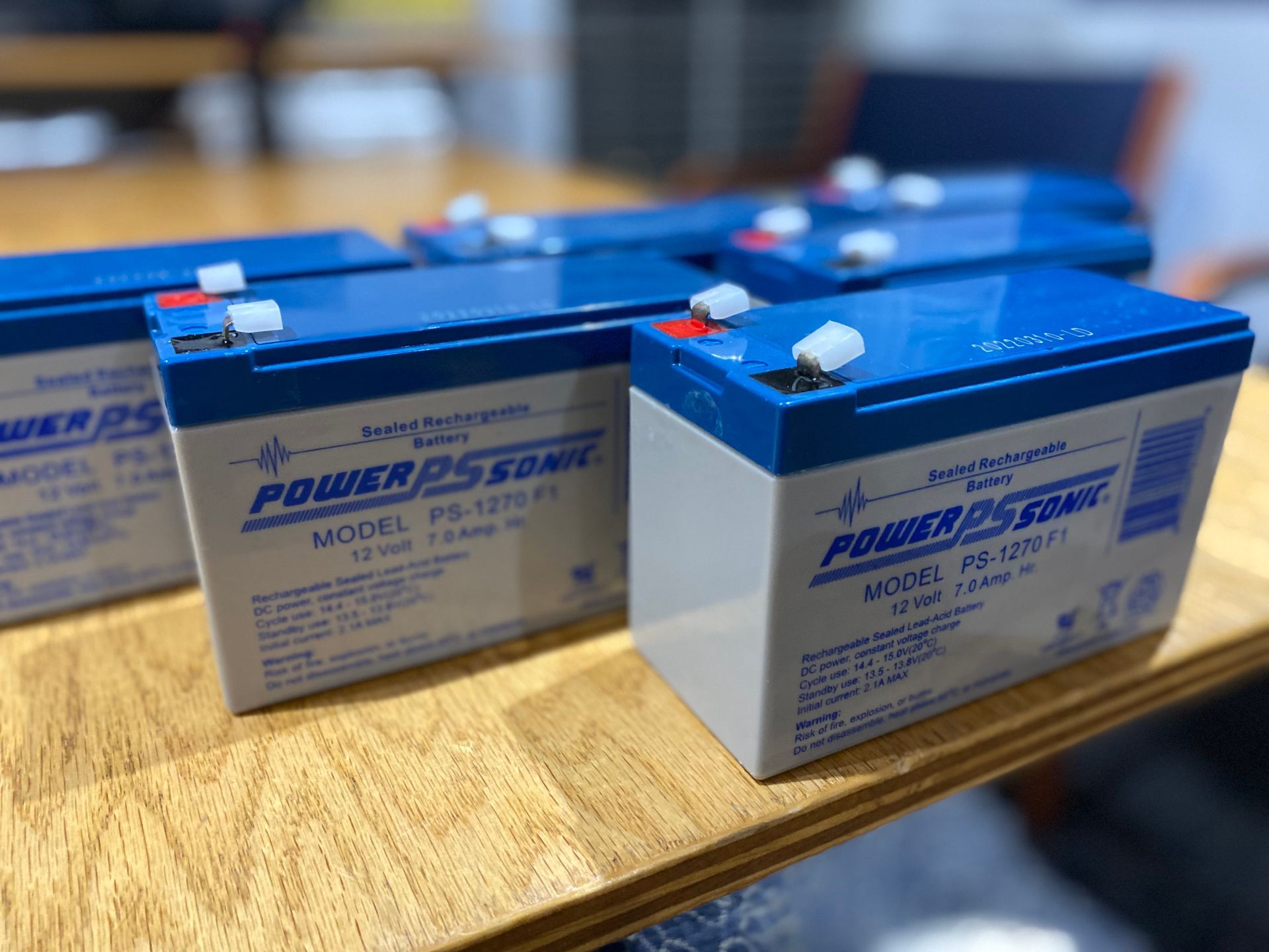 Several blue and white Power Sonic 12V batteries on a wooden surface.
