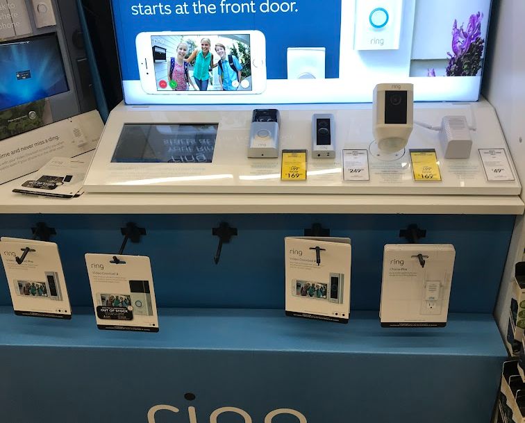 Ring doorbell display with various models on a blue shelf, store setting.