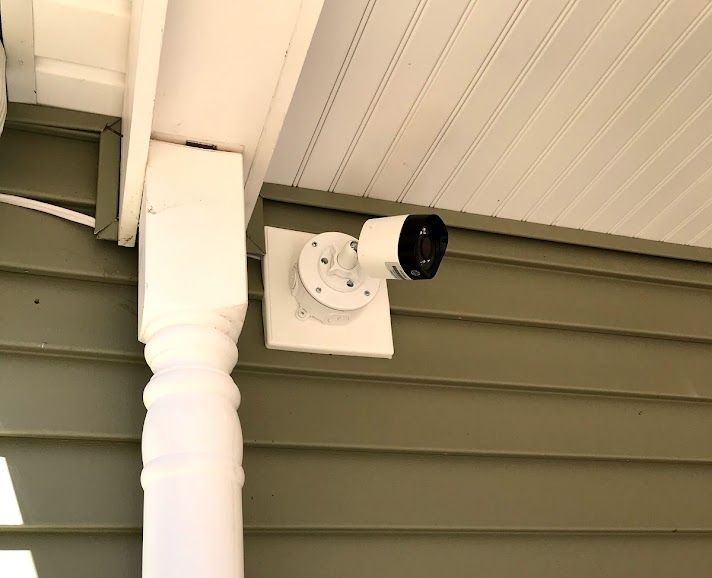 Security camera mounted on a white painted surface attached to a green house wall and porch.
