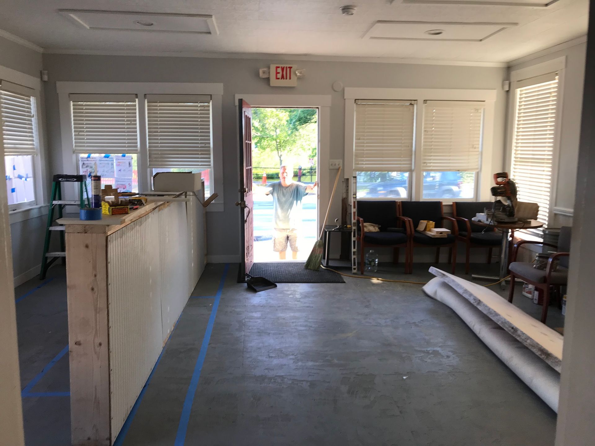 Interior of a room with a counter, open doorway, and a person standing outside; concrete floor.