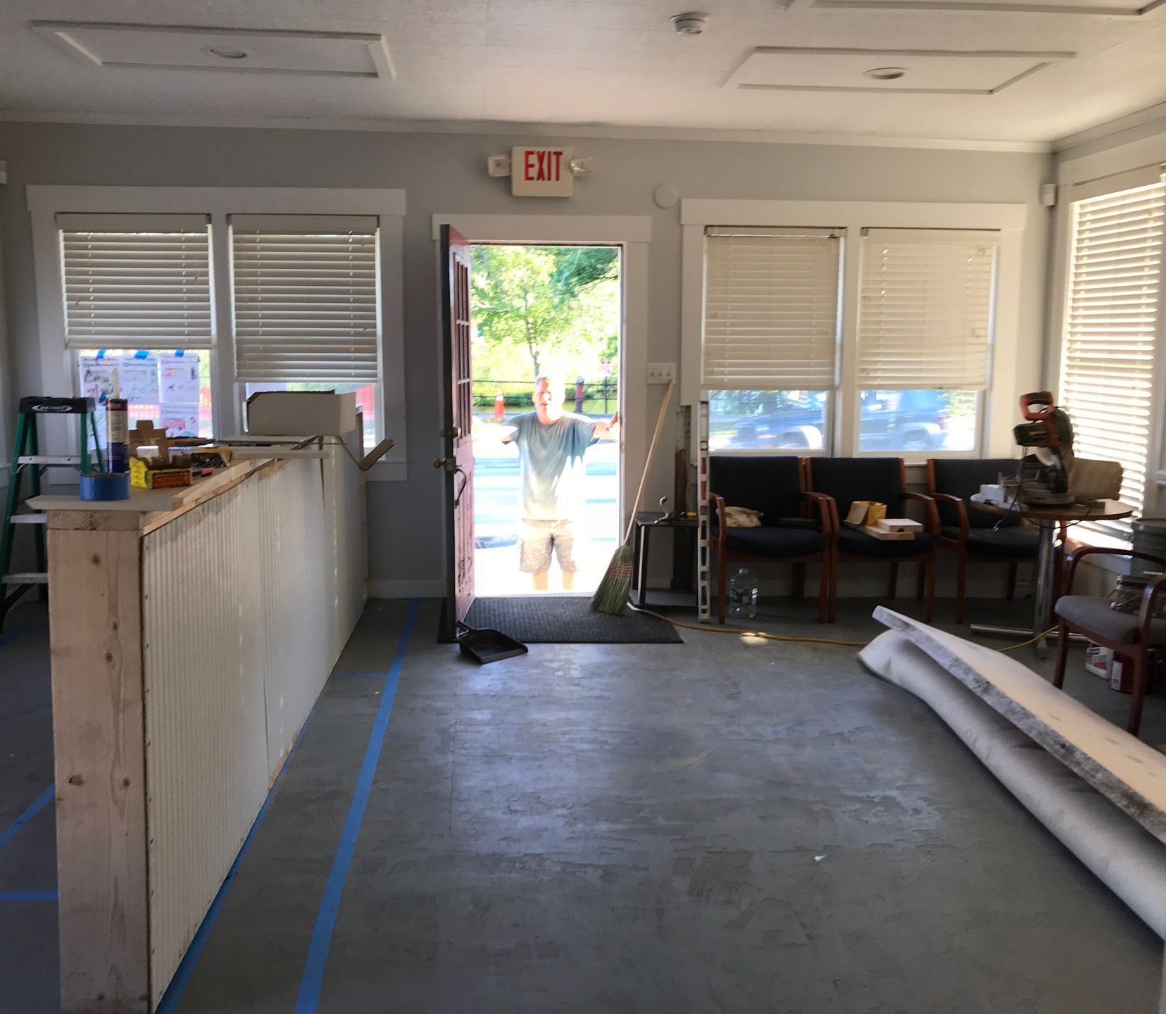 Open doorway with a person; a partially constructed counter and chairs in a room with windows.