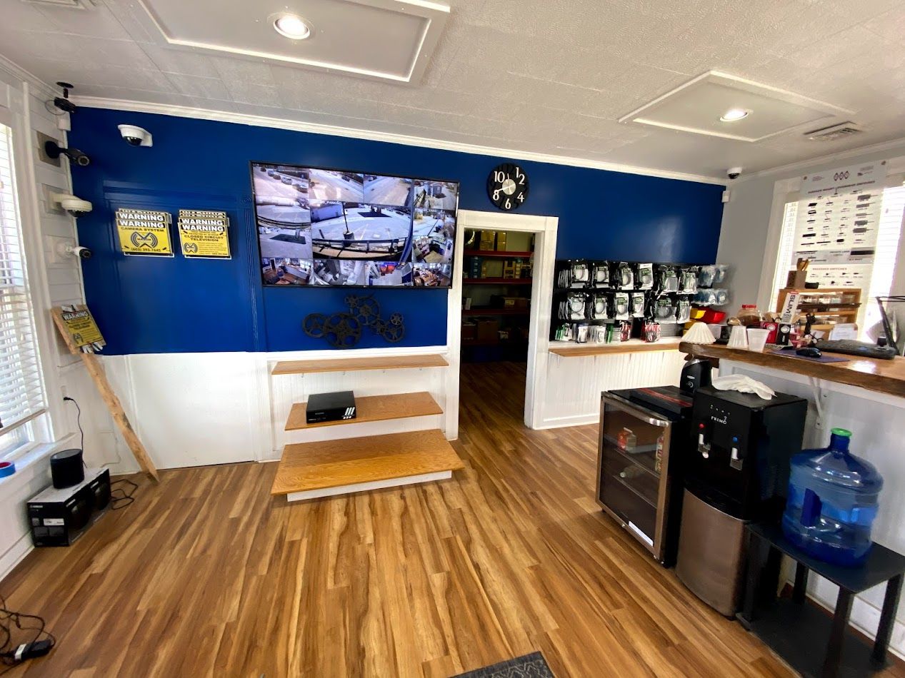 Interior of a security system business. Blue and white walls, monitor, wood floor, and security cameras for sale.