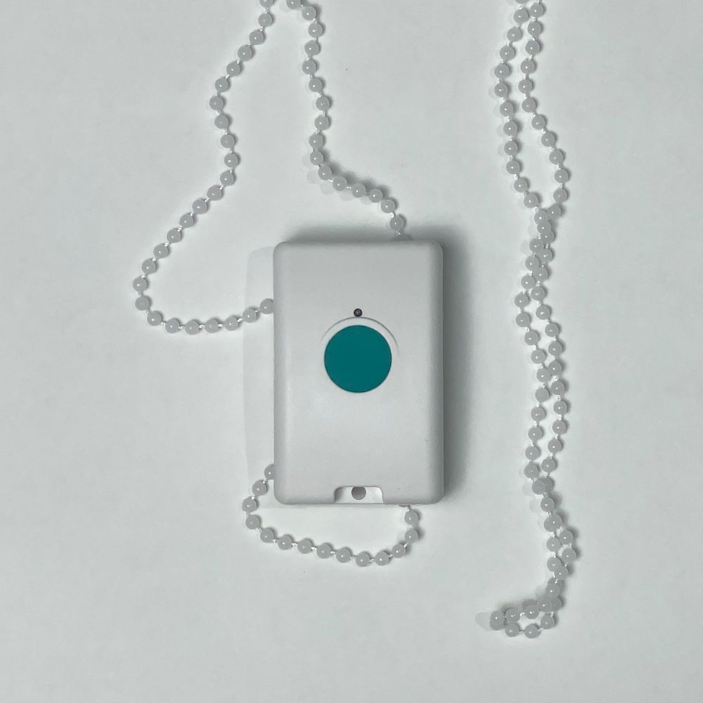 White emergency button with teal center, on a beaded chain, lying on white surface.