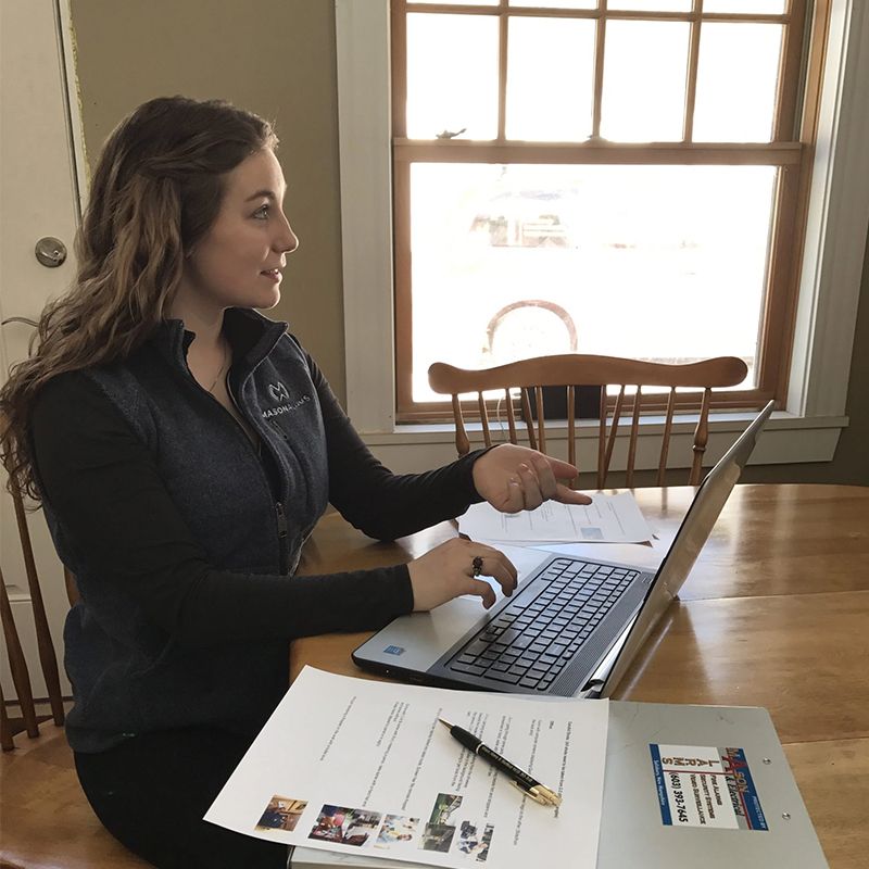 Woman working on a laptop at a table, pointing at a paper.