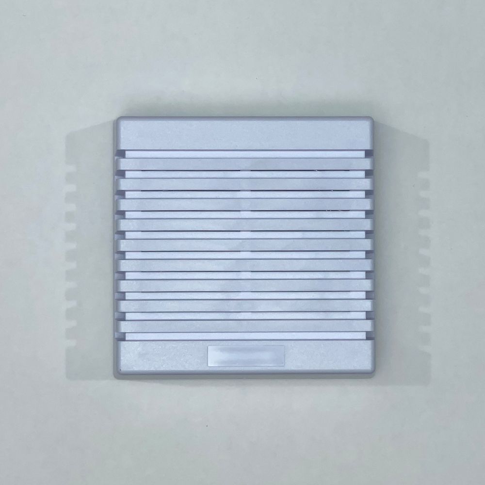 Silver, rectangular, horizontally-slatted speaker or vent on a light gray surface.