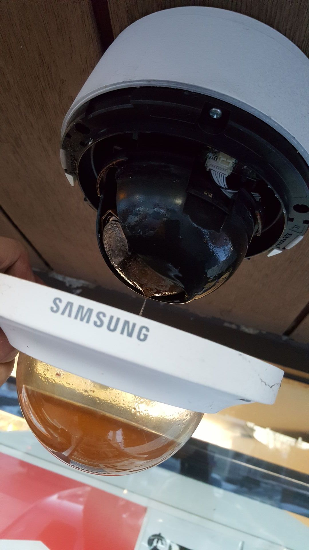 A damaged Samsung security camera with the dome cover removed, revealing internal components.