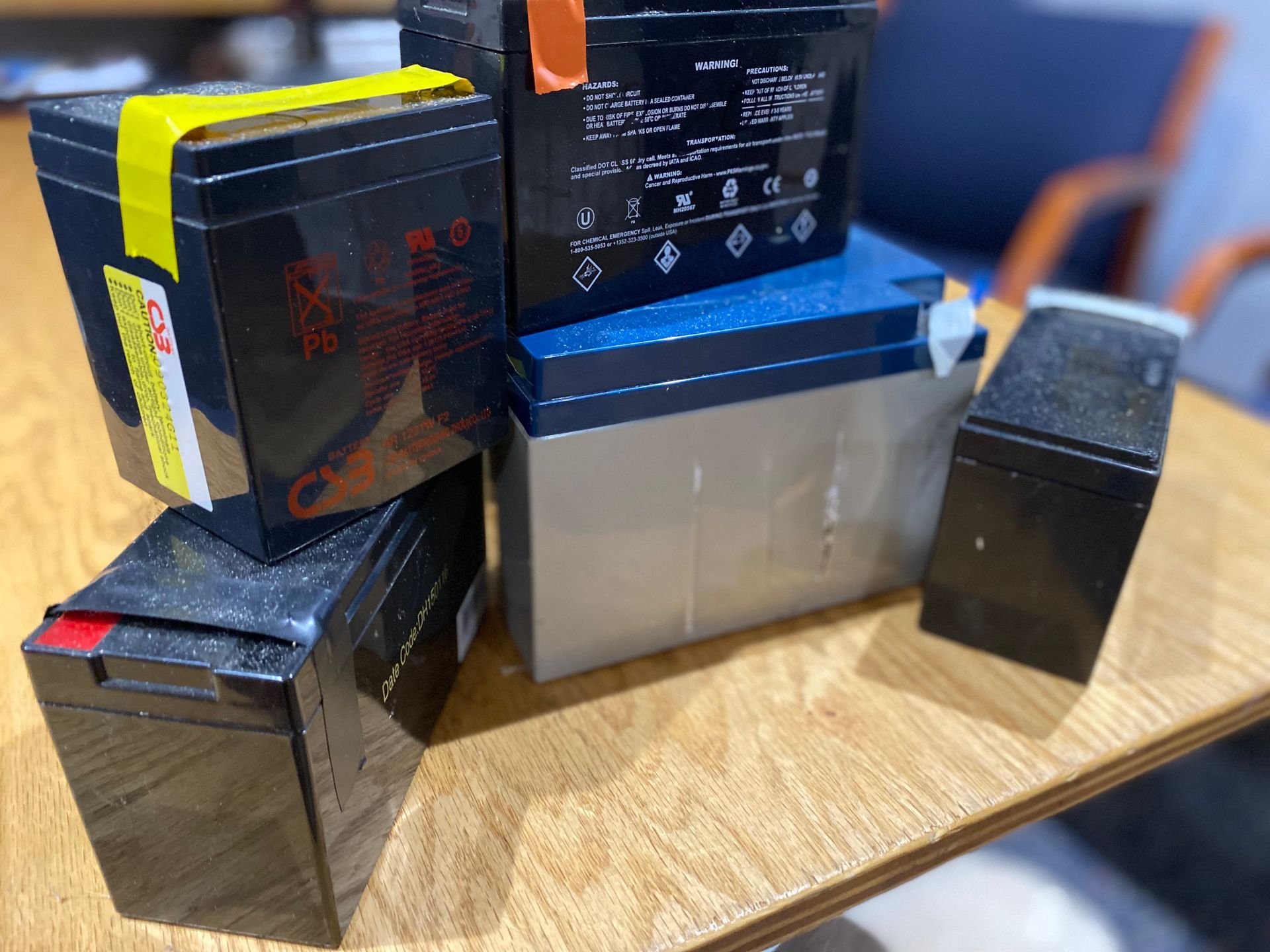 Stack of five rectangular black and silver batteries on a wooden table.