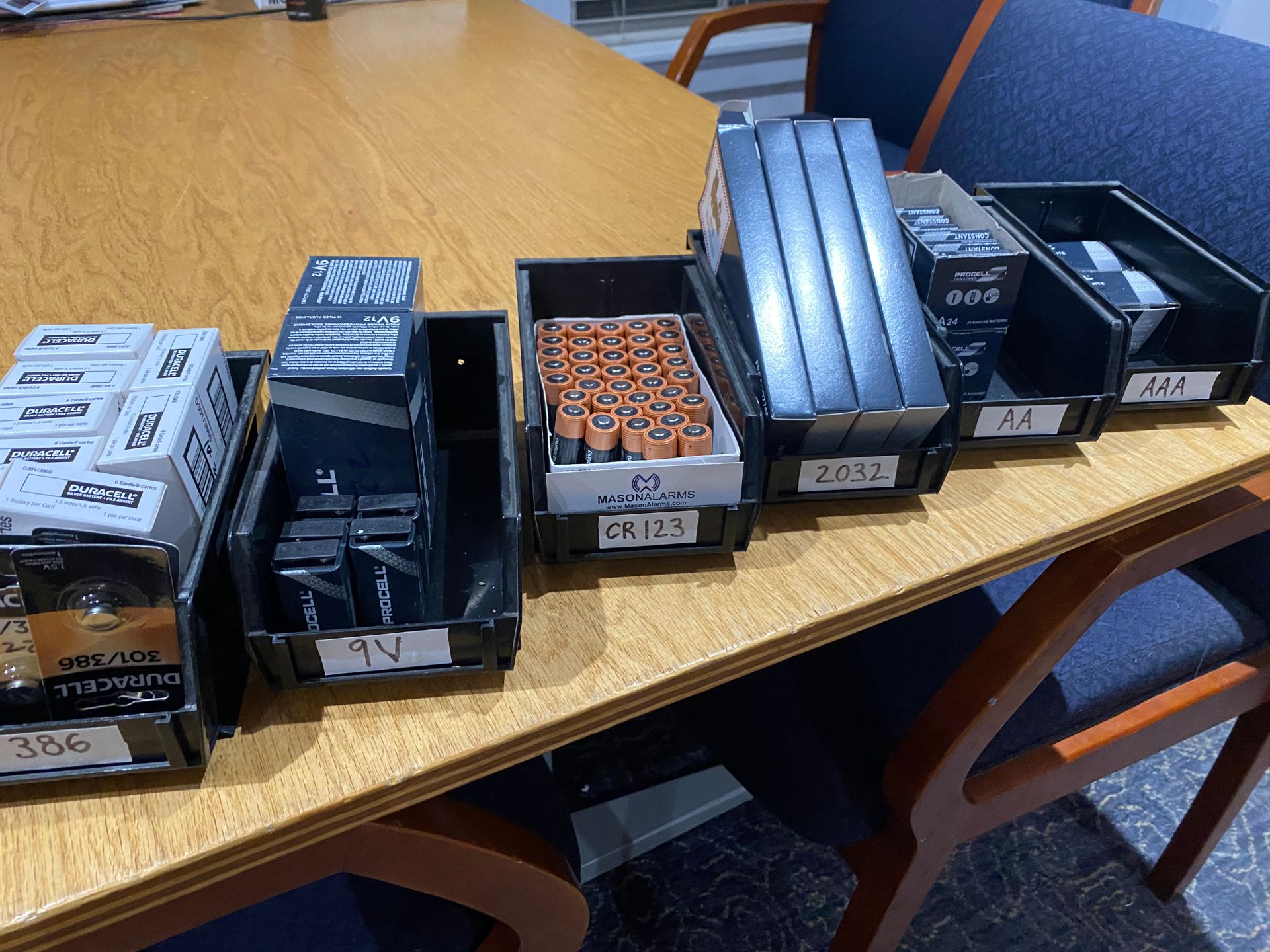 Six bins filled with various batteries sit on a wooden table.