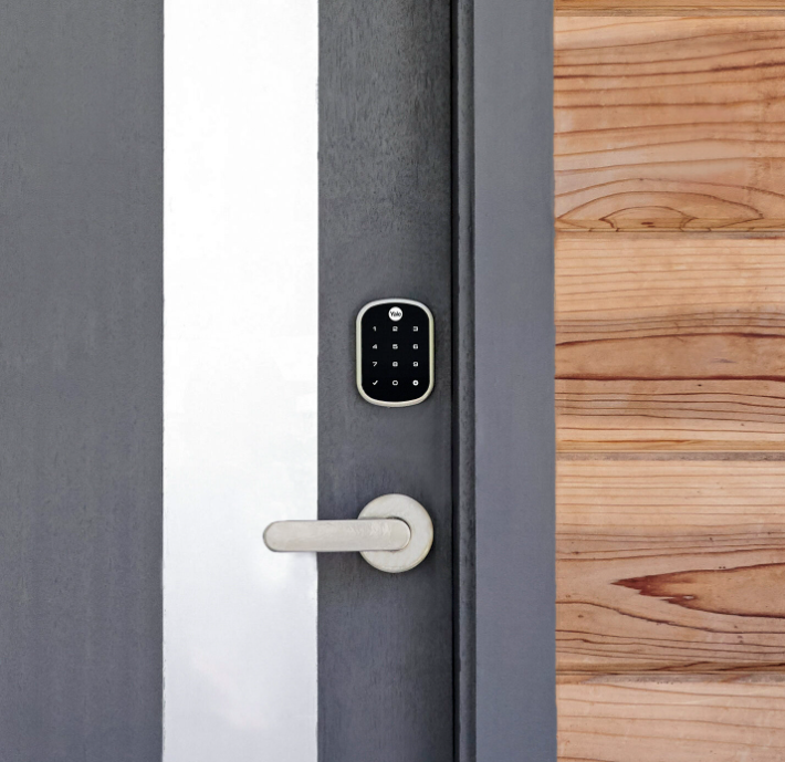 Black keypad smart lock and silver handle on a grey door with a wooden door beside it.