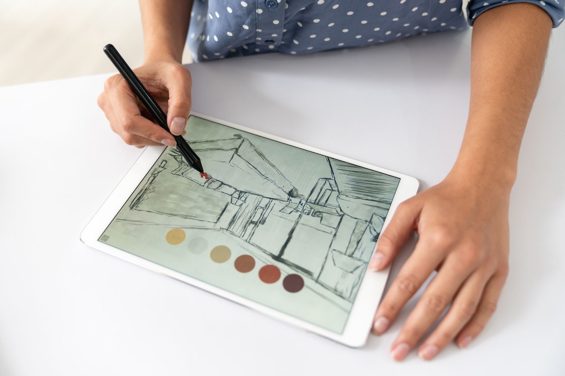 Person using a stylus to draw on a tablet, sketching an interior design with color swatches.