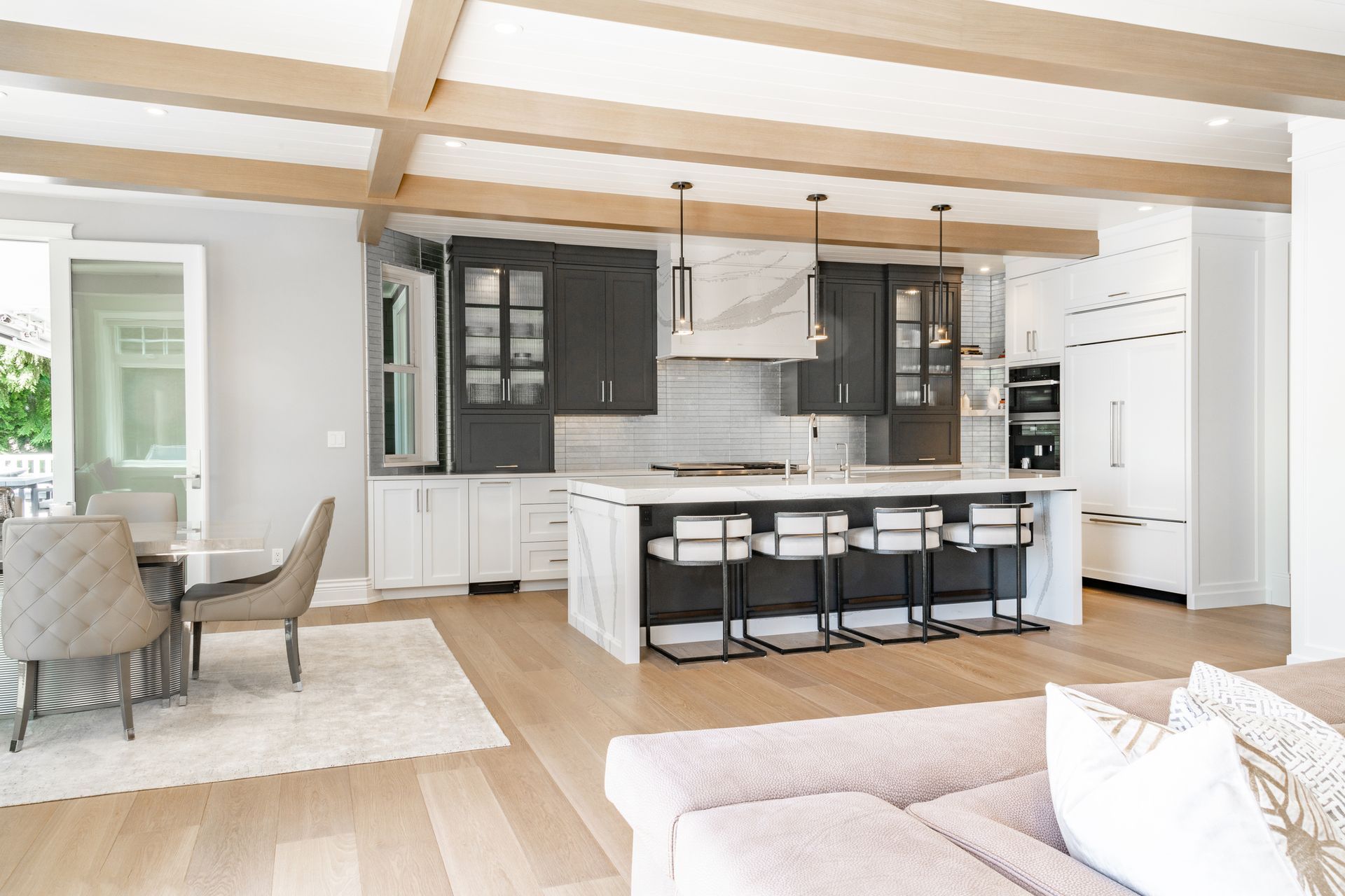 Modern kitchen with island, cabinets, and dining area; light wood floors and beams.